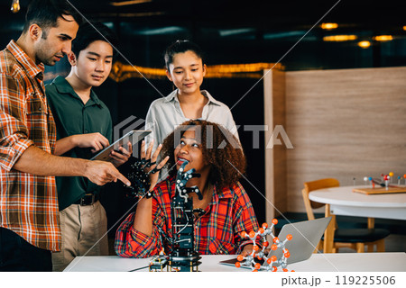 Engaged students and teacher learning together on a robotic arm in a classroom. Fostering innovation teamwork and practical education in a fun setting. Robot hand. Innovation and technology concept Engaged students and teacher learning together on a robotic arm in a classroom. Fostering innovation teamwork and practical education in a fun setting. Robot hand. Innovation and technology concept 119225506