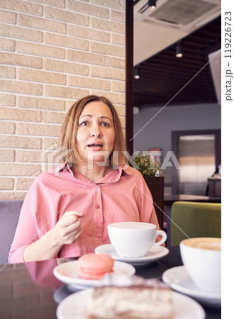 Surprised woman in cafe enjoying coffee and dessert against brick wall backdrop Surprised woman in cafe enjoying coffee and dessert against brick wall backdrop 119226723