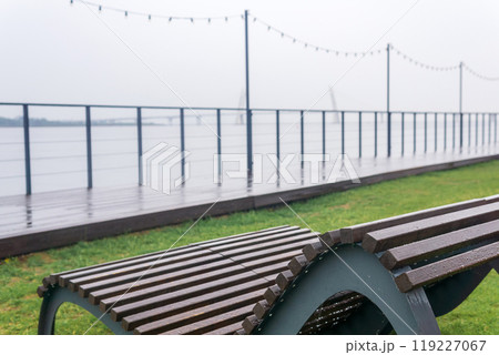bench in a public space on the embankment on the shore of a foggy bay with a bridge in the distance on a rainy day 119227067