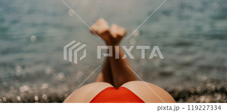 A woman sunbathes on the beach, lying on her stomach in a red swimsuit against the sea backdrop. 119227334