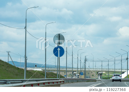 A road with a blue sign pointing to the right. The sky is cloudy and the road is empty. 119227368