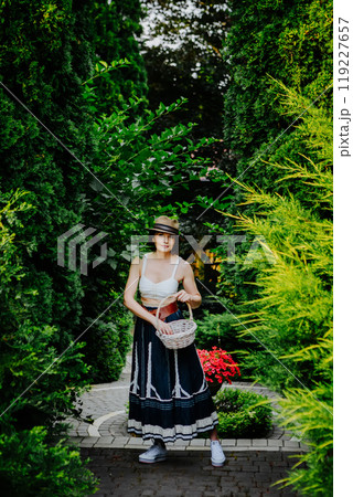 A woman in a stylish summer outfit and a striped sun hat is collecting eggs in a wicker basket A woman in a stylish summer outfit and a striped sun hat is collecting eggs in a wicker basket 119227657