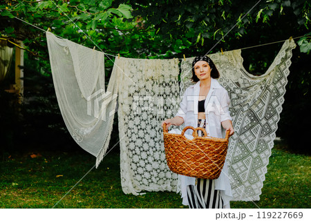 Woman stands in a lush green garden, hanging intricate lace fabric on a clothesline Woman stands in a lush green garden, hanging intricate lace fabric on a clothesline 119227669