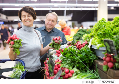 Mature woman and man selecting vegetables in greengrocer Mature woman and man selecting vegetables in greengrocer 119229481