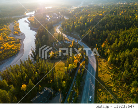 Aerial view of road along the river in the forest in autumn morning. Bow river and Three Sisters Parkway (Highway 742). Canmore, Alberta, Canada. 119235647