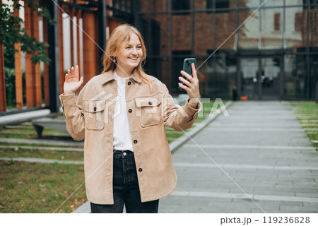 Laughing young woman taking selfie on the urban background. Cute beautiful woman using mobile phone. 30s girl recording self video, talking on online call 119236828