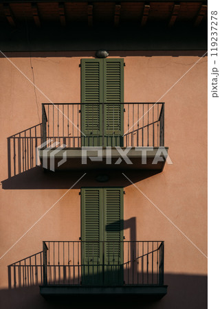 Charming Italian balconies adorned with lush green shutters and captivating shadows create an inviting atmosphere Charming Italian balconies adorned with lush green shutters and captivating shadows create an inviting atmosphere 119237278