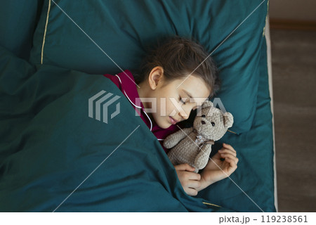 7 year old girl in red pajamas sleeps in green bed with her teddy bear toy 119238561