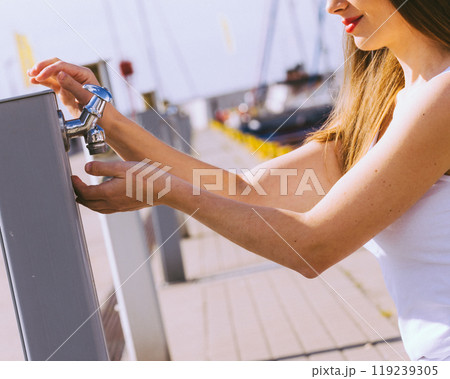 Woman drinking water from tap in marina. 119239305