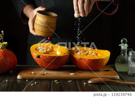 A chef adds salt to a cut ripe pumpkin on the kitchen counter before roasting. The concept is a low-key fruit diet or a national pumpkin dish 119239748