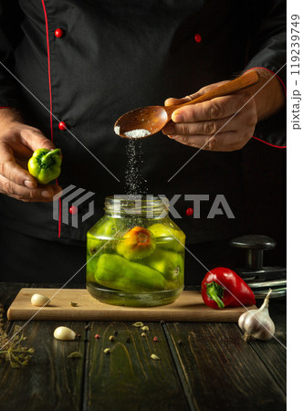 Preserving bell pepper with spices and garlic. A chef adds salt with a wooden spoon to a jar of pickled bell peppers. Advertising space on blackboards 119239749