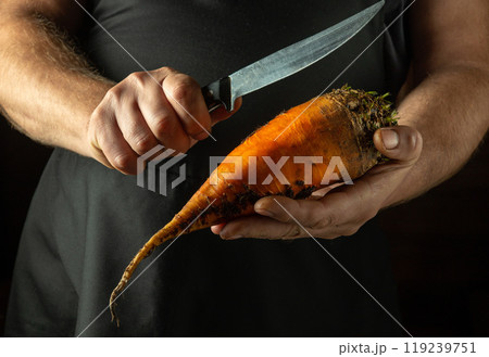 A cook cuts beets to add to food or borscht. Close-up of the chef hands holding an orange beet and a knife 119239751