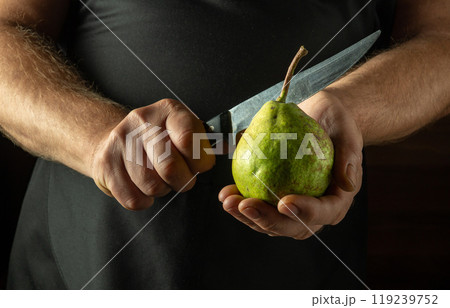 A chef tries to cut a green pear with a knife. Low key concept of making pear dessert in the kitchen 119239752