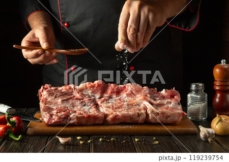 Chef sprinkles raw lamb meat with salt. Preparing a large steak of raw meat before roasting. Working environment in a hotel kitchen Chef sprinkles raw lamb meat with salt. Preparing a large steak of raw meat before roasting. Working environment in a hotel kitchen 119239754