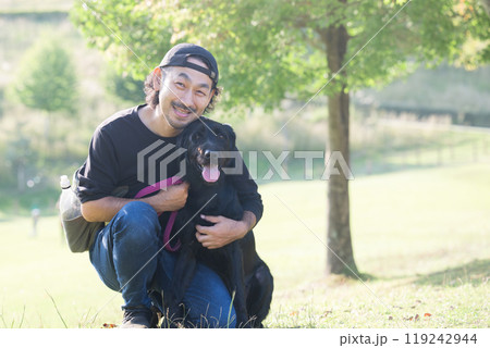 緑がきれいな場所でペットの大型犬と飼い主の男性とカメラ目線の全身 コピースペースあり 緑がきれいな場所でペットの大型犬と飼い主の男性とカメラ目線の全身 コピースペースあり 119242944