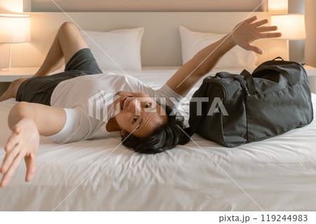 Happy traveler man lying on the hotel bed with luggage travel bag. 119244983