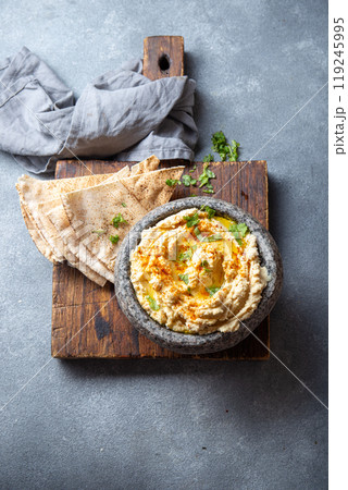 Traditional Jewish hummus served in a stone bowl, garnished with olive oil, paprika, and parsley, alongside flatbreads and fresh herbs on a gray table Traditional Jewish hummus served in a stone bowl, garnished with olive oil, paprika, and parsley, alongside flatbreads and fresh herbs on a gray table 119245995