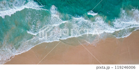 Aerial view of a sandy beach with turquoise waves crashing onto the shore scattered people are seen walking along the coastline 119246006
