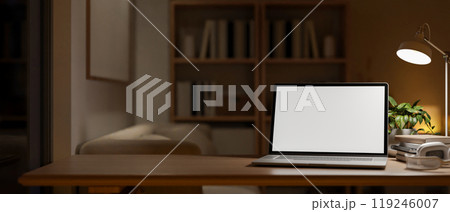 A close-up of a laptop on a wooden table in a modern apartment at night, illuminated by a table lamp A close-up of a laptop on a wooden table in a modern apartment at night, illuminated by a table lamp 119246007