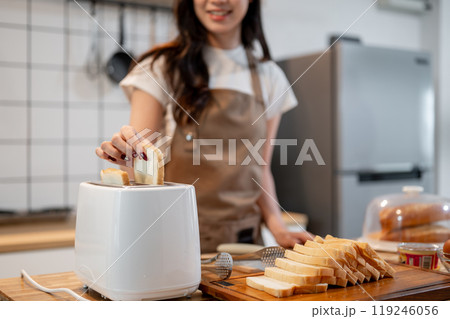A close-up of a woman putting a slice of bread in a toaster, making toast in the kitchen. A close-up of a woman putting a slice of bread in a toaster, making toast in the kitchen. 119246056