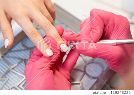 Nail technician carefully paints gel polish on woman nails using a small brush Nail technician carefully paints gel polish on woman nails using a small brush 119248226