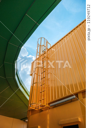 Vertical view ofFire escape stairs on buildings is constructed with metal sheet material painted in yellow throughout with a background of a blue sky during the day. Vertical view ofFire escape stairs on buildings is constructed with metal sheet material painted in yellow throughout with a background of a blue sky during the day. 119249712