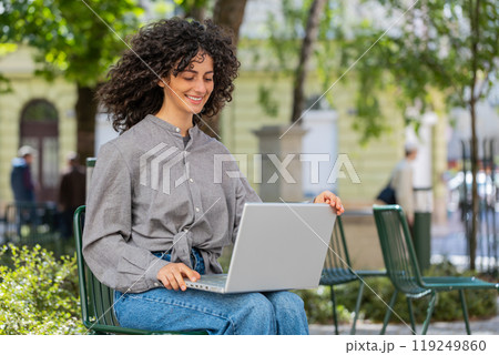 Woman freelancer working online distant job with laptop browsing website sitting on city street 119249860