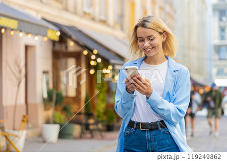 Happy woman using smartphone typing texting social media application messages e-mail on city street Happy woman using smartphone typing texting social media application messages e-mail on city street 119249862