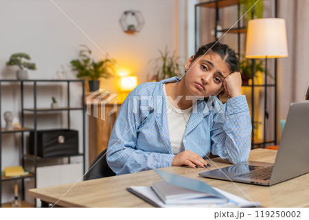 Sad Indian young woman freelancer looks pensive thinks over life concerns sitting at desk at home Sad Indian young woman freelancer looks pensive thinks over life concerns sitting at desk at home 119250002