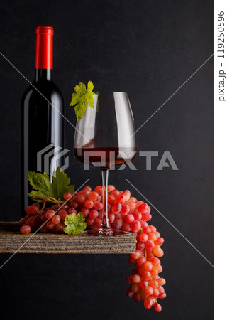 A glass and bottle of wine paired with grapes, set against a dark background 119250596