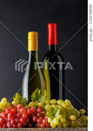 Bottles of red and white wine paired with grapes, set against a dark background Bottles of red and white wine paired with grapes, set against a dark background 119250600