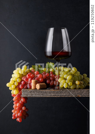 A glass of wine paired with grapes, set against a dark background 119250602