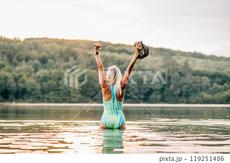 Cold water swimming for elderly woman. Rear view of senior sporty woman standing in lake during cold morning. Cold water swimming for elderly woman. Rear view of senior sporty woman standing in lake during cold morning. 119251486