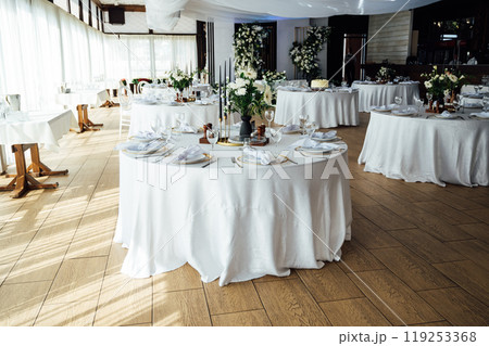 Luxurious restaurant. Luxurious interior, white tables, serving dishes and glasses for guests Luxurious restaurant. Luxurious interior, white tables, serving dishes and glasses for guests 119253368