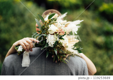 The bride and groom are hugging. The bride hugs the groom's neck and holds her bouquet of flowers The bride and groom are hugging. The bride hugs the groom's neck and holds her bouquet of flowers 119253689