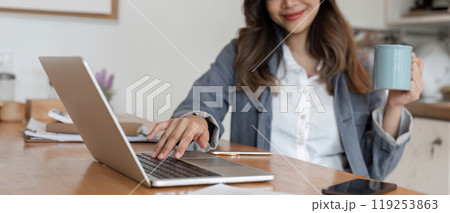 Young Female Freelancer Working Online from Home with Laptop and Coffee in Modern Home Office Setting 119253863