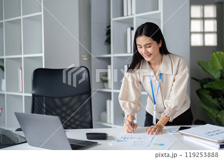 Businesswoman Analyzing Data and Working on Laptop in Modern Office Environment with Shelves and Plants Businesswoman Analyzing Data and Working on Laptop in Modern Office Environment with Shelves and Plants 119253888