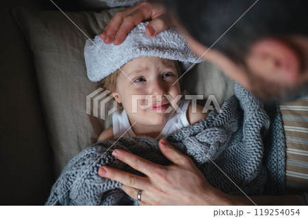 Father taking care of sick son with fever and cold, holdig cold cloth to his forehead. Boy lying on sofa, feeling tired. Top view. 119254054