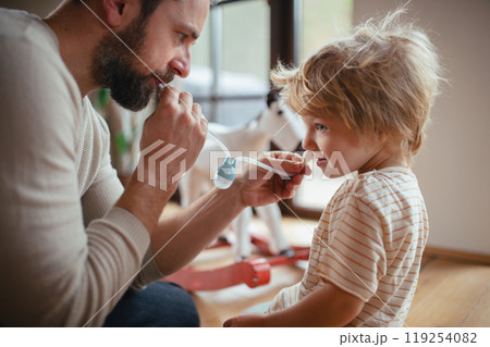 Father helping son with stuffy nose, using nasal suction bulb to clear mucus from his nose. 119254082