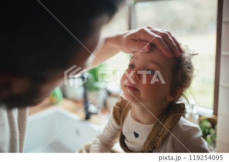 Sick girl with fever and cold at home. Father touching little daughter forehead, checking her temperature. 119254095