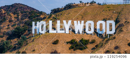 The Hollywood Sign is displayed on Mount Lee's hills, with white letters against dry terrain and shrubs, under a clear sky in Los Angeles. The Hollywood Sign is displayed on Mount Lee's hills, with white letters against dry terrain and shrubs, under a clear sky in Los Angeles. 119254096