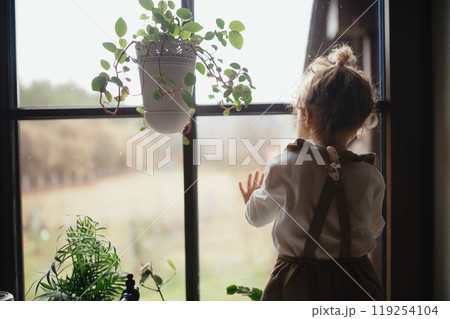 Portrait of an adorable little girl sitting on the kitchen counter, looking out of window. 119254104