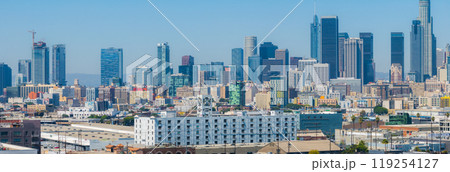 The image captures an aerial view of downtown Los Angeles, showcasing modern skyscrapers like the U.S. Bank Tower and Wilshire Grand Center against a clear blue sky. 119254127