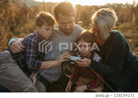 Portrait of family sitting in the middle of meadow. taking photos with vintage camera. Portrait of family sitting in the middle of meadow. taking photos with vintage camera. 119254131