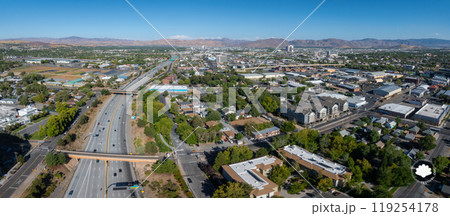 Aerial perspective of Reno, Nevada, featuring urban sprawl, a prominent highway, and surrounding mountains under a clear blue sky in daylight. 119254178