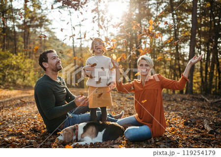 Young family with small children and dog on a walk in autumn forest. Throwing dry colorful leaves in the air. Young family with small children and dog on a walk in autumn forest. Throwing dry colorful leaves in the air. 119254179