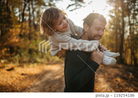 Father and girl are playful during walk in autumn forest. Dad and girl having fun outdoors. Father and girl are playful during walk in autumn forest. Dad and girl having fun outdoors. 119254186