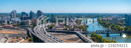 Aerial view of Sacramento, California, highlighting the golden Tower Bridge, the Ziggurat building, modern skyline, and lush greenery along the river. 119254221