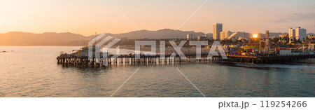 Santa Monica Pier extends into the Pacific Ocean, featuring a Ferris wheel and amusement park. The cityscape and mountains are visible in the background. 119254266