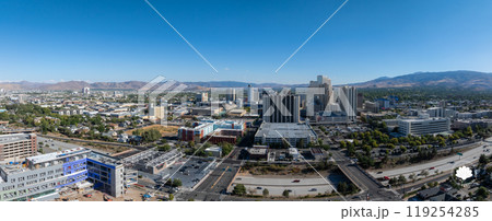 Reno, Nevada's urban landscape is seen from above, featuring high rise casino hotels, residential areas, and distant mountains under a clear blue sky. 119254285